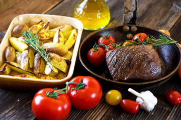 Delicious beef steak with potato on wooden background.
