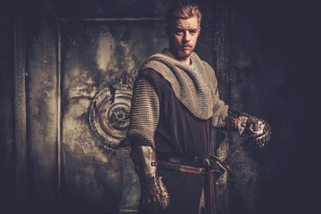 Young medieval knight standing on dark background.