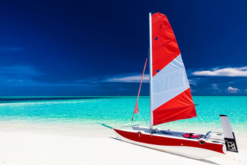 Sailing boat with red sail on a beach of deserted tropical islan
