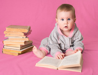 Adorable baby girl with old books reading on pink background. 