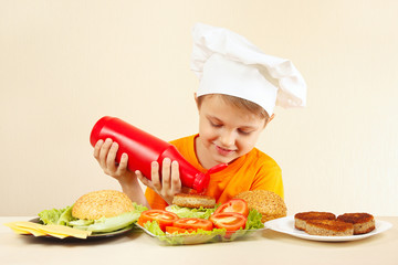 Little funny chef puts ketchup on the hamburger