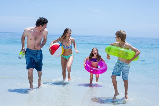 Cheerful family running in shallow water with swimming equipment