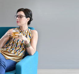 Trendy woman having tea sitting in blue armchair