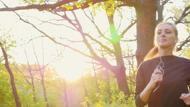 Steadicam slow motion shot: Healthy life - a woman jogging on a spring forest, listening to music