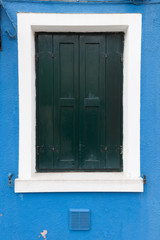 Obraz na płótnie Canvas Old window with dark green shutters on blue wall