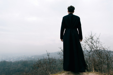 Fototapeta premium Portrait of handsome catholic bearded man priest or pastor posing outdoors in mountains