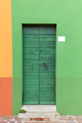 Old wooden green locked door with peeling paint in the green wal