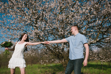 Naklejka na ściany i meble Beautiful young couple dancing and having fun on blue sky background in bloom garden,lifestyle