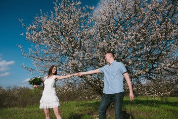 Naklejka na ściany i meble Beautiful young couple dancing and having fun on blue sky background in bloom garden,lifestyle