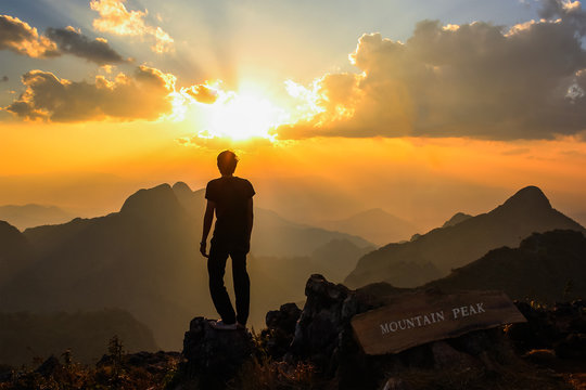 Man standing on mountain peak at sunset.