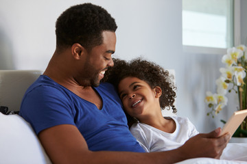 Black father and daughter relaxing in bed look at each other