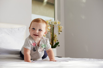 A happy baby girl crawling on a bed, copy space on right
