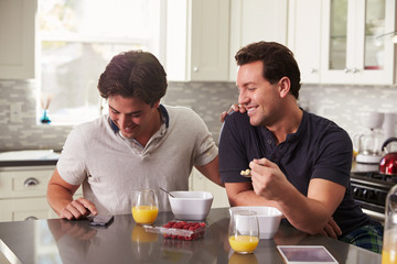Male gay couple looking at smartphone over breakfast