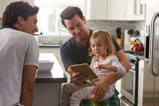 Male gay couple using tablet with their daughter in kitchen