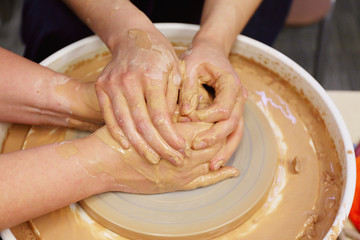 woman potter helps student how to hold hands in the manufacture of the vessel on the potter's wheel