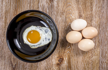 Fresh and fried eggs on wooden background