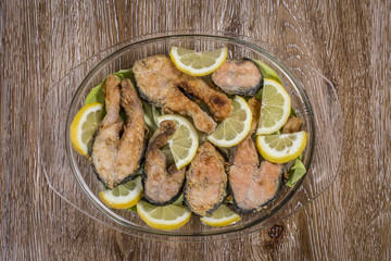 Fried fish ( with sliced lemon ) in a plate on wooden background