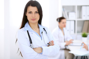Brunette female doctor on the background of colleagues talking to each other in hospital
