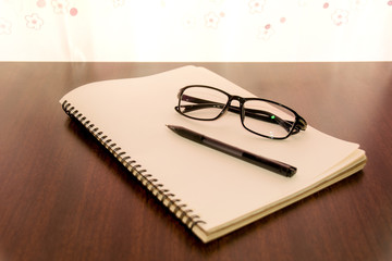 Pen glasses and notebook on wood table