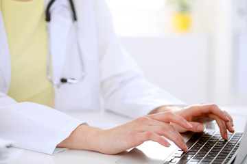 Close-up of female doctor typing laptop sitting at a table in the hospital