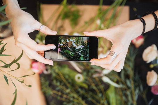 Florist holding smartphone and taking photos of flower on table