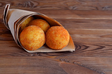 Arancini. Fried rice balls in paper on brown wooden background. Snack, sicilian street food