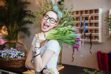 Happy woman florist holding bunch of purple tulips and winking