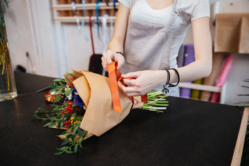 Woman florist making flower bouquet with red ribbon in shop