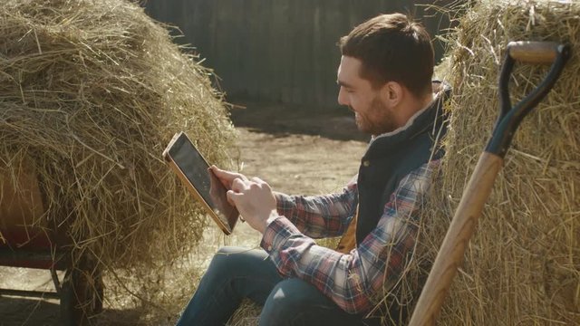 Man is sitting in hay and using a tablet computer. Shot on RED Cinema Camera.