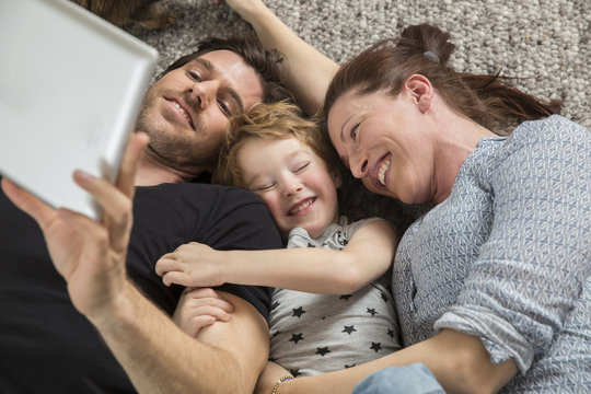 Happy family lying on floor, using digital tablet
