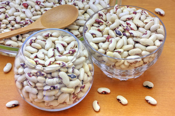 Colorful haricot beans in glass bowls on wooden background
