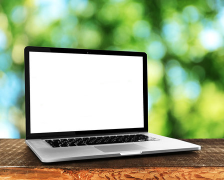 Laptop over wooden table on natural  green blurred background