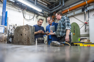 Three men in factory discussing workpieces