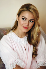 Beautiful blonde bride in vintage robe posing on sofa