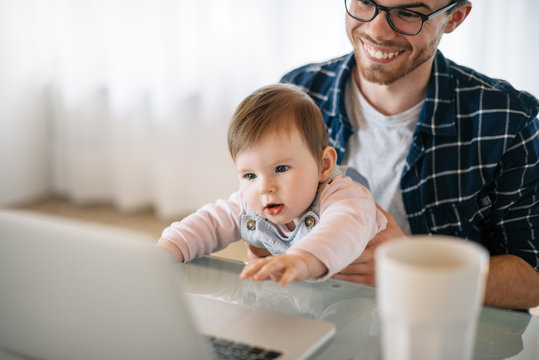 Portrait of baby girl sitting on father's lap looking at laptop