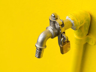 Yellow faucet on yellow wall with padlock prevent water theft. Concept of save water.