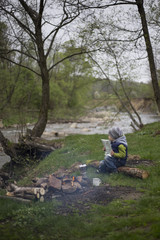 Teenager sitting near a fire in camping and watching map.