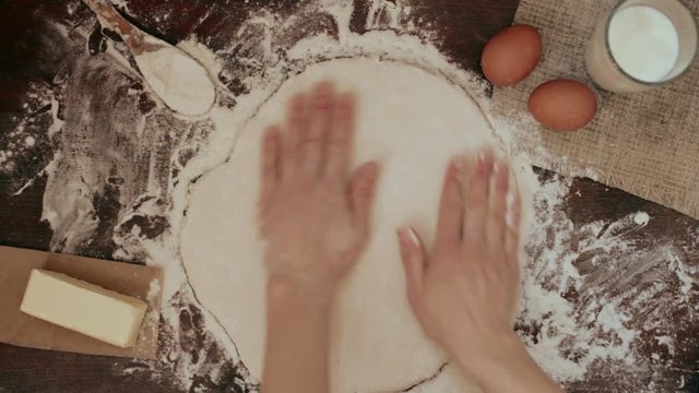 Female chef rolling pizza dough on wooden table with spread flour. Concept of Italian meal preparation. 