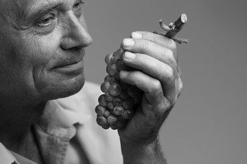 Old man holding a grape in his hand