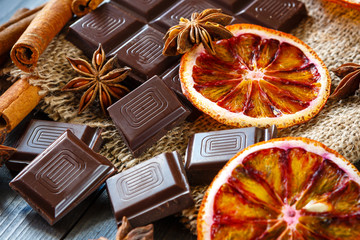 Dark chocolates with dry oranges, cinnamon and anise on burlap on rustic table