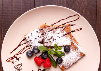 Honeyed cake with ginger dusted with icing sugar with raspberry, bilberry, mint on  plate on wooden background. Top view.