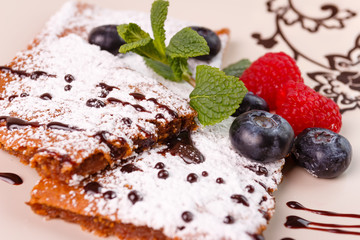 Honeyed cake with ginger dusted with icing sugar with raspberry, bilberry, mint on  plate on wooden background