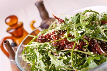 Green healthy salad with arugula and sun-dried tomatoes and parmesan cheese on a wooden kitchen table. Pepper, peppermoll, utensils for olive oil, vinegar and seasonings. Italian cuisine