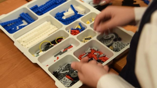 Boy taking some details to make a robot. Working with educational kit at robotics class at school
