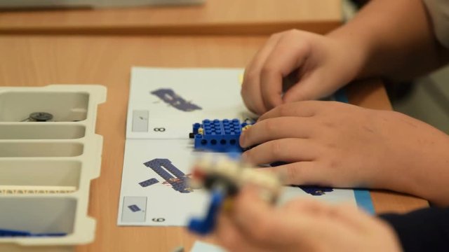 Two boys pupils making robots following the instruction of educational kit. Studying robotics at school