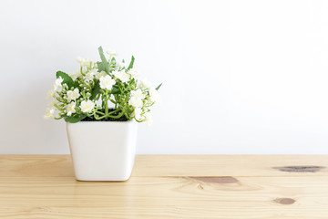 the artificial jasmine flower in the pot at the wooden table with the white wallpaper