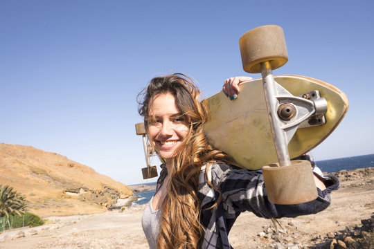 Spain, portrait of smiling teenage girl with longboard on shoulders