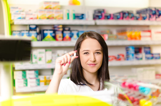 Pharmacist chemist woman show a pill. Pharmacy drugstore is background. Pretty, young woman. Pharmaceutical.