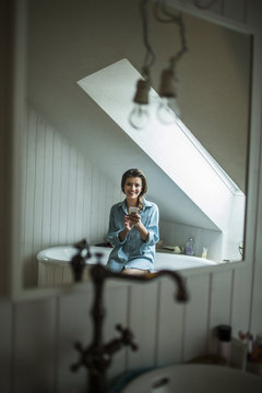 Young woman in bathroom using smartphone