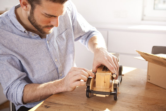 Young man sitting at table with wooden toy car